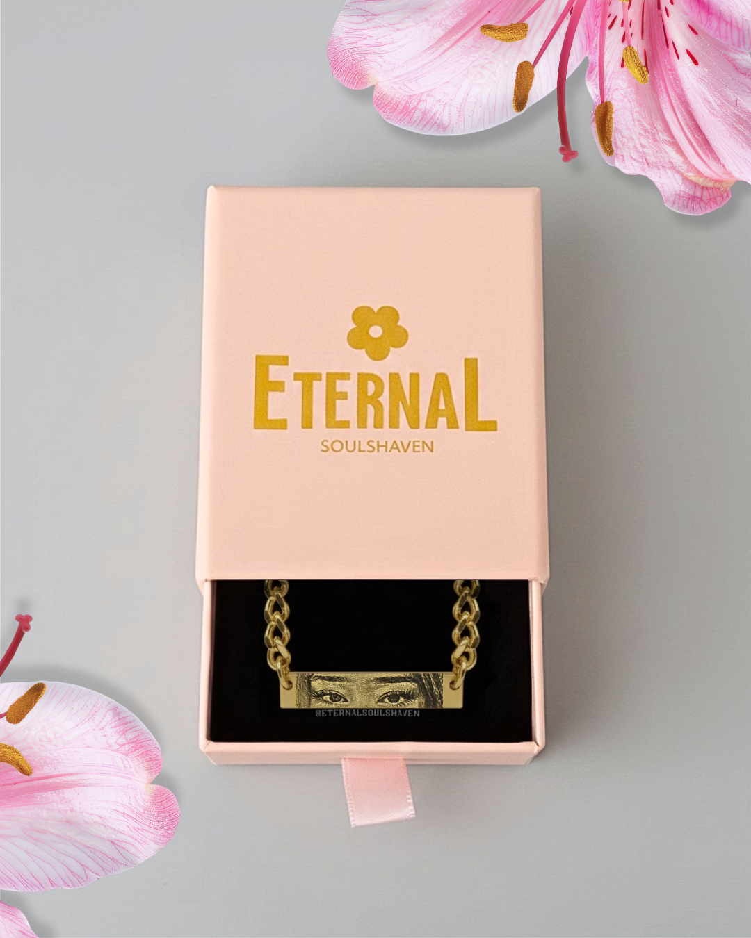 Gold necklace in a 'Eternal Soulshaven' box with pink flowers on a gray background